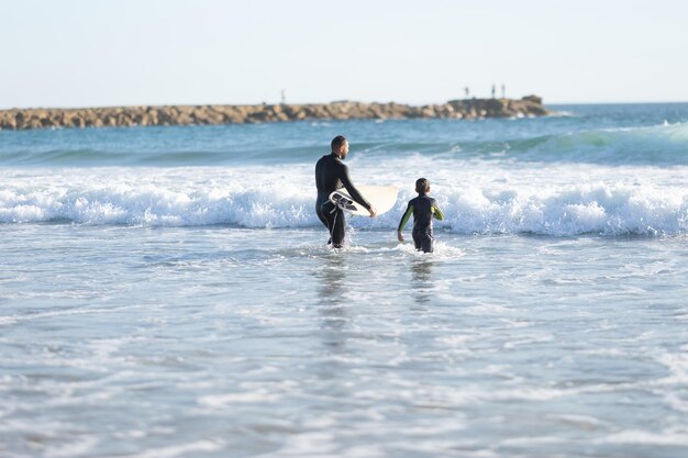 Une famille de surfeurs père et fils en combinaison va en mer