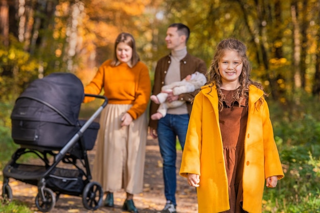 Une famille traditionnelle heureuse se promène dans le parc d'automne avec des enfants et une poussette par beau temps