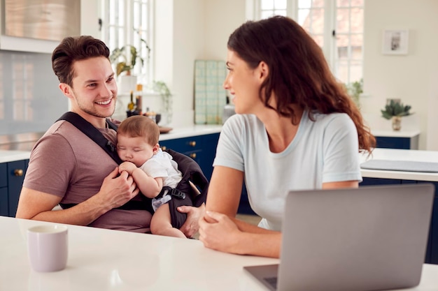 Famille transgenre avec bébé travaillant à domicile regardant un ordinateur portable sur le comptoir de la cuisine