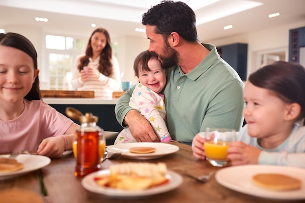 Famille trisomique Fille assise autour d'une table à la maison en train de prendre son petit déjeuner