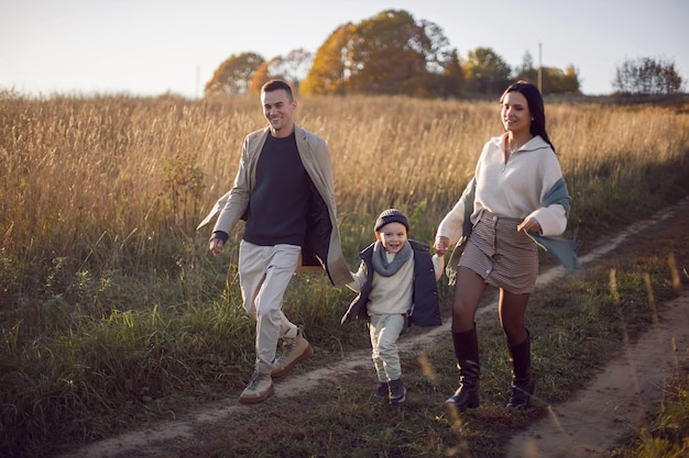 Photo famille de trois personnes avec un garçon maman et papa courent sur un champ en automne au coucher du soleil