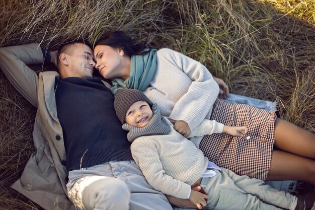 Famille de trois personnes avec un garçon, maman et papa sont allongés sur un champ en automne au coucher du soleil