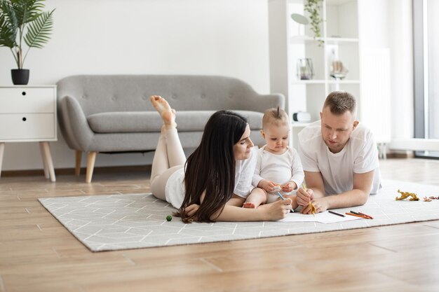 Famille de trois personnes posant avec des crayons à dessin sur le sol à l'intérieur