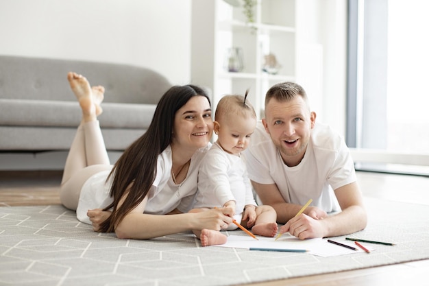 Famille de trois personnes posant avec des crayons à dessin sur le sol à l'intérieur