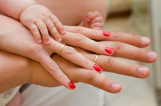 Une famille de trois personnes tient main dans la main la petite main de bébé sur la main de maman et de papa