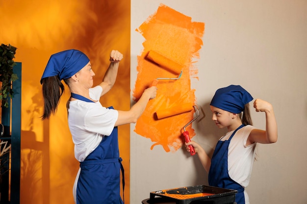 Famille utilisant la couleur orange pour peindre les murs de l'appartement à la maison, peindre la salle avec une brosse à rouleaux et des outils de rénovation. Femme avec petit enfant redécorant la maison, amélioration de la décoration.