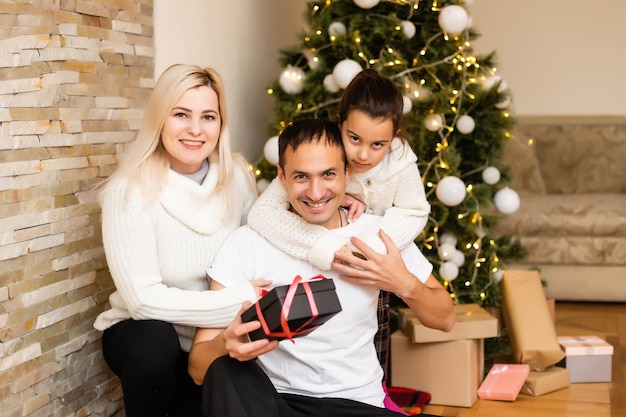 famille, vacances et personnes - mère souriante, père et petite fille sur fond de lumières d'arbre de noël