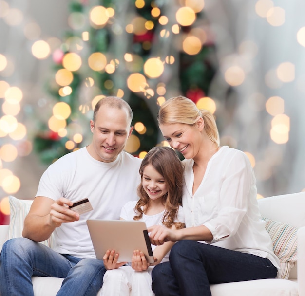 famille, vacances, shopping, technologie et personnes - famille souriante avec ordinateur tablette et carte de crédit sur fond de lumières de sapin de noël