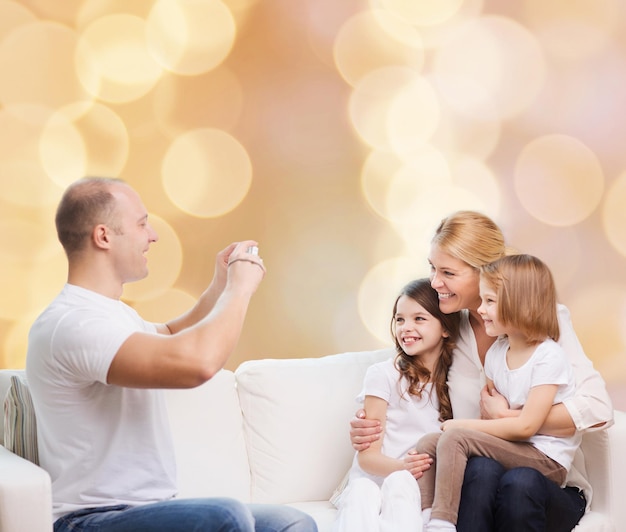 famille, vacances, technologie et personnes - mère souriante, père et petites filles avec caméra sur fond de lumières beiges