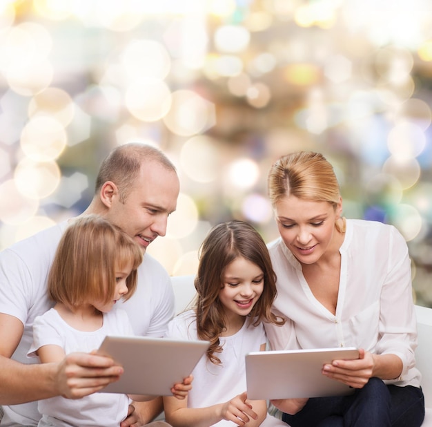 famille, vacances, technologie et personnes - mère souriante, père et petites filles avec des ordinateurs tablettes sur fond de lumières