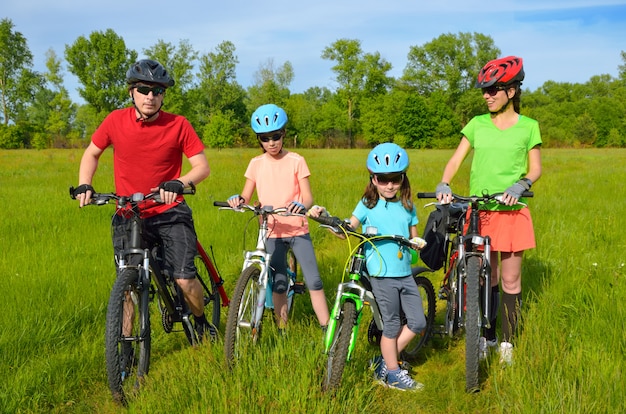 Famille à vélo à l'extérieur, heureux parents actifs et deux enfants à vélo sur la prairie de printemps, sport, fitness et concept de mode de vie sain