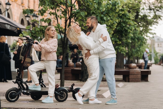 Une famille en vêtements blancs se tient dans la ville sur des scooters électriques