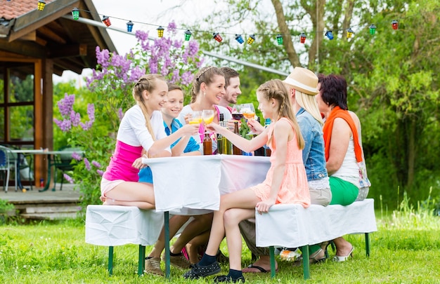 Famille et voisins à la garden-party en train de boire, assis devant une maison avec des amis et la famille