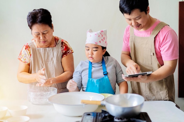Les familles asiatiques s'entraident dans la cuisine fille père et grand-mère papa utilise une tablette pour voir comment cuisiner