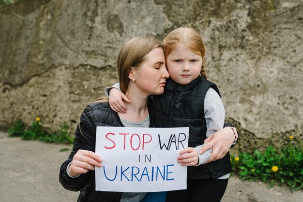 Familles contre la guerre Portrait petit enfant bouleversé avec la mère appelle Pas de guerre lève une bannière avec inscription Arrêtez la guerre en Ukraine Paix arrêtez l'agression russe Espoir pour le monde Evacuation des civils