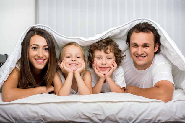 Familles avec enfants au lit sous une couverture.