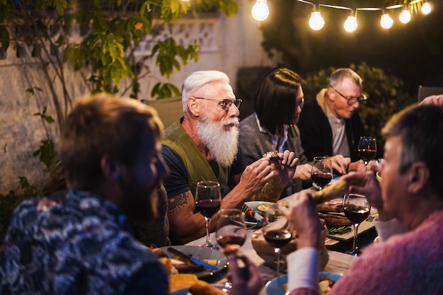 Familles mangeant au dîner barbecue - Amis multiraciaux savourant un repas en plein air - Concept de nourriture, d'amitié, de rassemblement et de mode de vie estival - Focus sur le visage de l'homme hipster