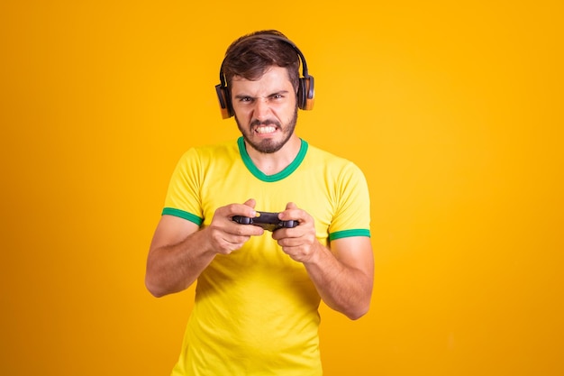 Fan brésilien de football ou de football portant un uniforme jaune et tenant un contrôleur de jeu vidéo sur fond jaune
