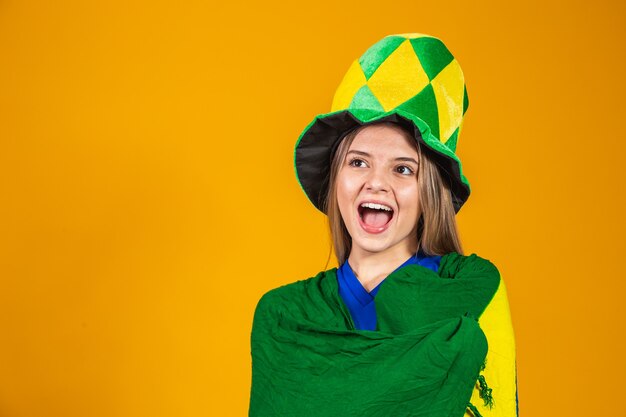 Fan brésilienne blonde célébrant sur fond jaune avec le drapeau du Brésil