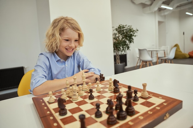 Fan d'échecs motivé garçon caucasien à l'air excité tout en jouant aux échecs assis à la table dans