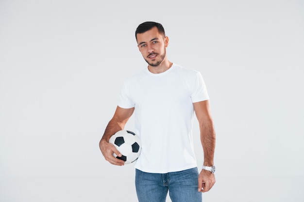 Fan de football avec ballon de soccer Jeune bel homme debout à l'intérieur sur fond blanc