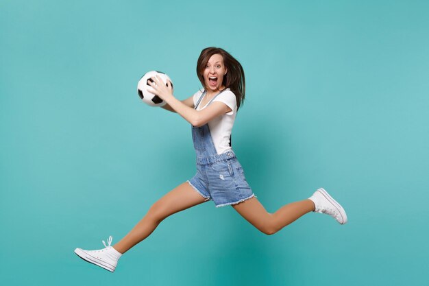 Fan de football femme folle égayer l'équipe préférée de soutien tenant un ballon de football sautant isolé sur fond bleu turquoise. Émotions des gens, concept de mode de vie de loisirs familiaux sportifs. Maquette de l'espace de copie.