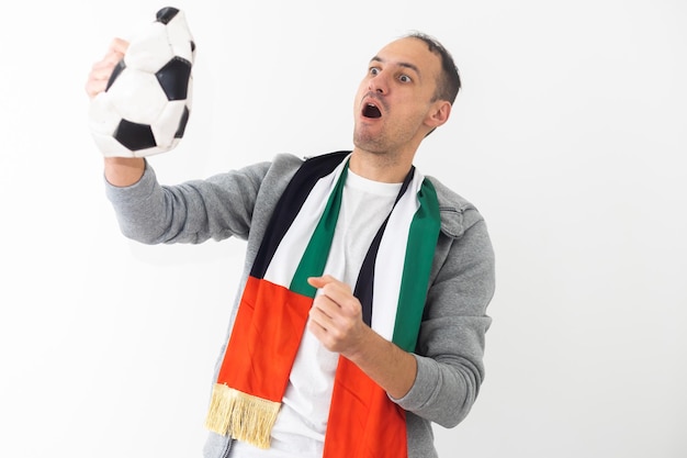 Fan de football. Un gars émotionnel criant célébrant la victoire de l'équipe tenant le ballon posant sur fond de studio. Photo de haute qualité