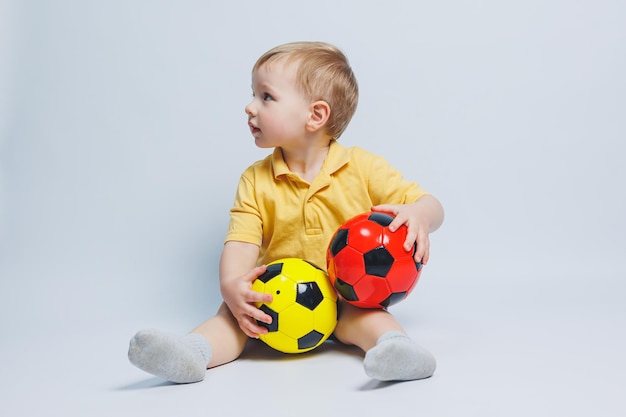 Fan de garçon tenant un ballon de football dans ses mains isolé sur fond blanc Enfant débutant dans le sport de football pour les enfants Petit athlète Kit de football jaune et bleu pour les enfants