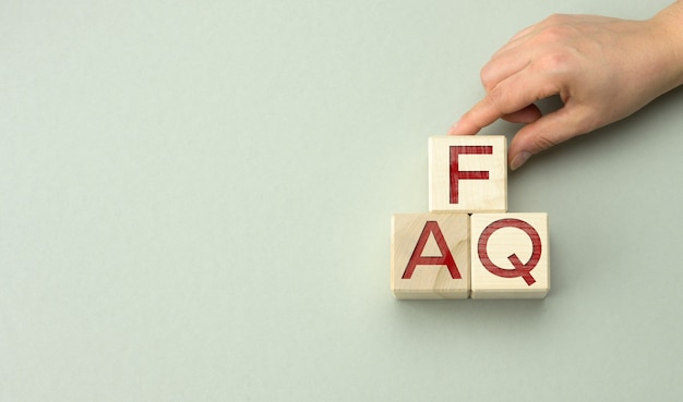 FAQ d'inscription (questions fréquemment posées) sur des blocs de bois sur une surface grise. Concept d'assurance qualité, aide et conseils, mains tenant des cubes, espace de copie