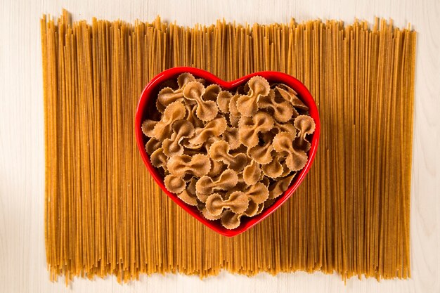 Farfalle intégral dans un bol coeur sur des spaghettis