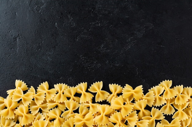 Farfalle pâtes crues sur table en béton noir. Concept de cuisine. Vue de dessus avec espace de copie.