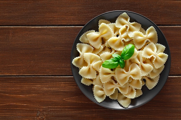 Farfalle pâtes cuites au basilic feuilles vertes sur fond de table en bois marron vue de dessus de l'espace pour copier textxA