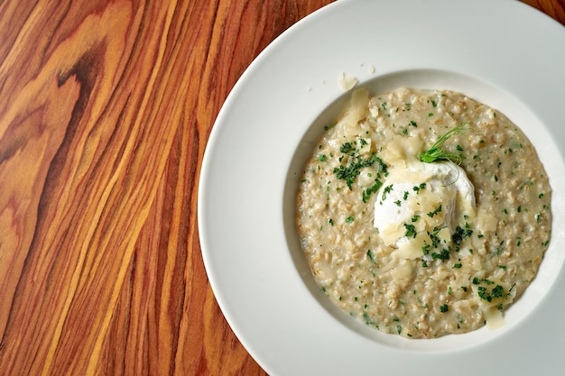 Farine d'avoine avec parmesan et œuf poché dans une assiette blanche sur un fond en bois