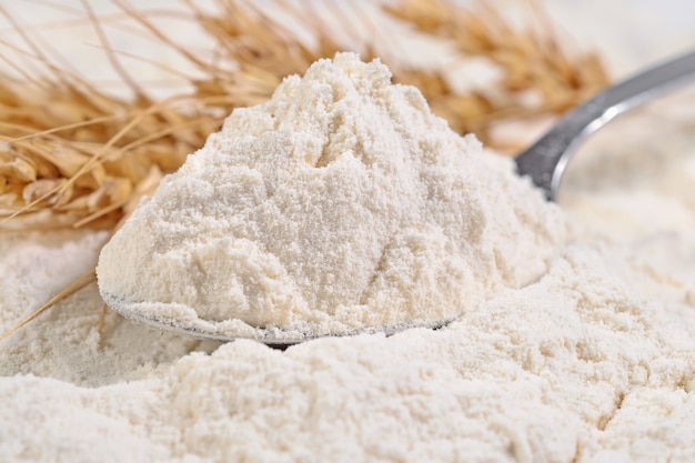 Farine blanche dans une cuillère et épis de blé se bouchent