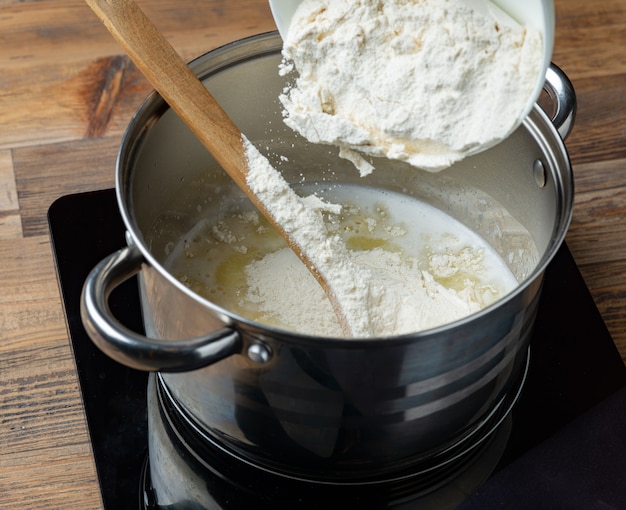 La farine est versée dans une casserole avec de l'eau chaude et du beurre pour faire de la pâte à éclair