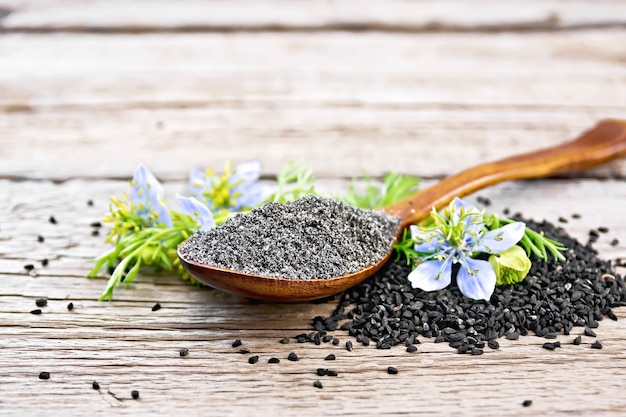 Farine de Nigella sativa en cuillère avec une fleur et des feuilles de kalingini sur fond d'une vieille planche de bois