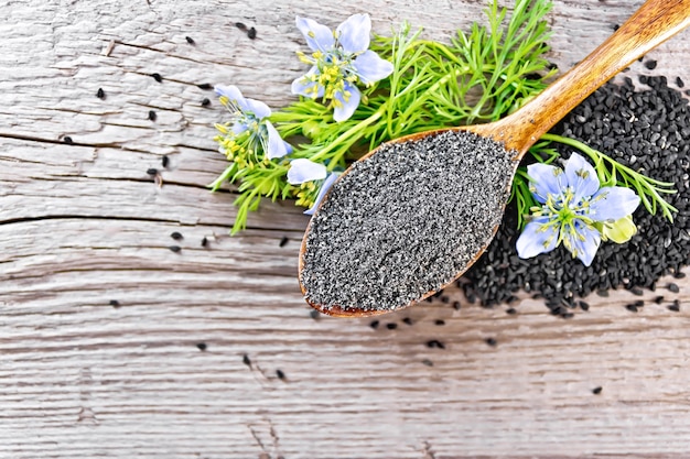 Farine de Nigella sativa en cuillère avec une fleur et des feuilles de kalingini sur une d'une vieille planche de bois d'en haut