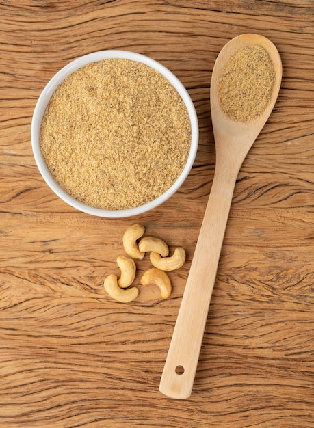 Farine de noix de cajou dans un bol et dans une cuillère sur une table en bois. Farine sans gluten.