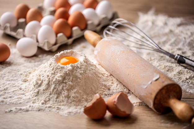 Farine avec oeuf à côté d'un rouleau en préparation d'une pâte sur une surface en bois