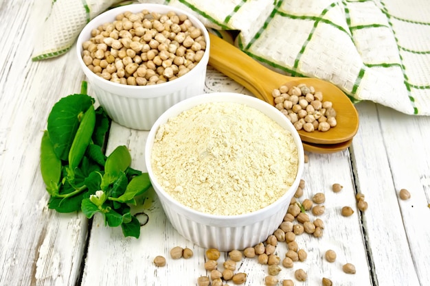 Farine de pois chiches et de pois chiches dans des bols et des cuillères blancs, des gousses de haricots verts, une serviette sur un fond de planches de bois