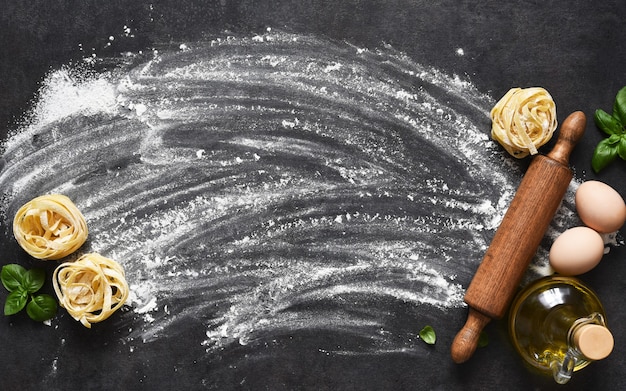 Farine, rouleau à pâtisserie, tomates et basilic sur la table.