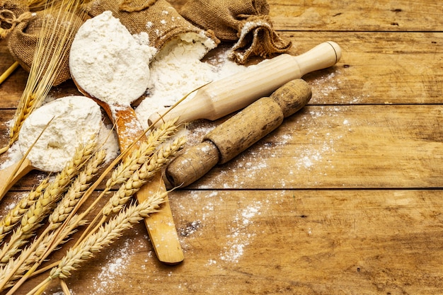 Farine en sacs, épis de céréales, cuillères et rouleaux à pâtisserie en bois. Concept de cuisson, table en bois, espace copie