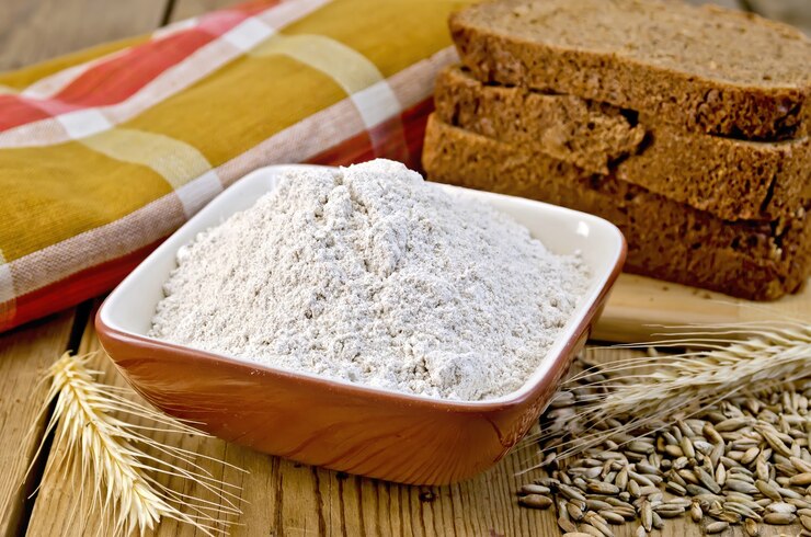 Photo farine de seigle dans un bol, miches de pain de seigle maison, épillets et grain de seigle, serviette sur planche de bois