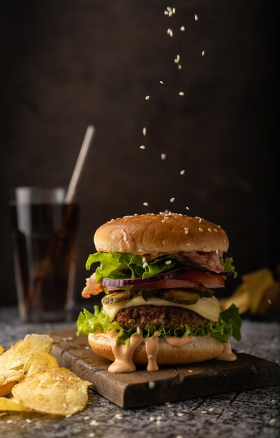 Fast food. un grand burger juteux avec galette de boeuf, laitue iceberg, tomates, cornichons, oignons et sauce et tranches de bacon. Ambiance sombre et discrète