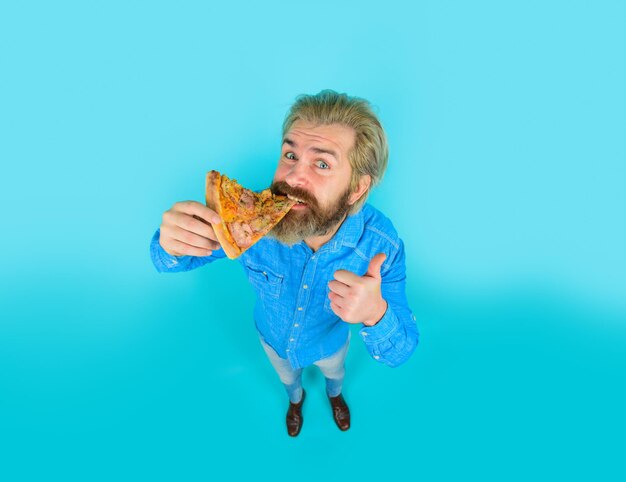 Fast food homme mangeant de la pizza montre le pouce vers le haut pizzeria homme barbu mange une tranche de pizza cuisine italienne