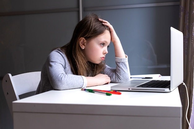 Fatigué des cours d'informatique en ligne, une fille regarde le moniteur avec tristesse à la maison