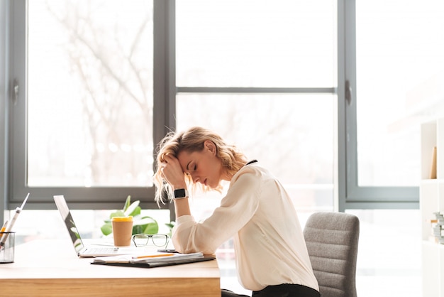 Fatigué de jeune femme d'affaires assis au bureau à l'aide d'un ordinateur portable