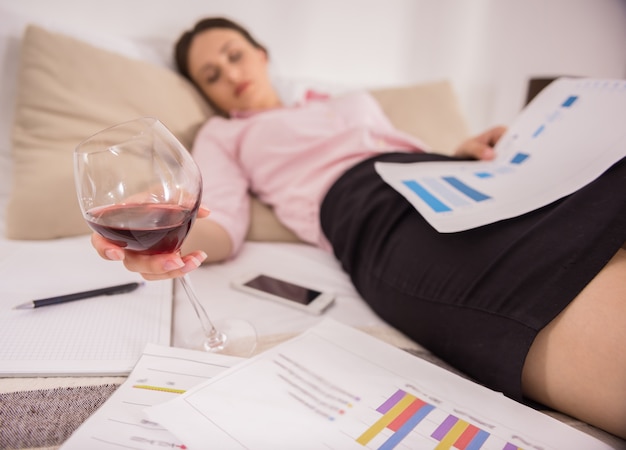 Fatigué de jeune femme endormie sur le lit avec un verre de vin.