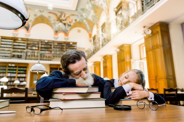 Fatigué senior barbu professeur professeur et son élève ou petite-fille dorment dans une bibliothèque se trouvant sur la table