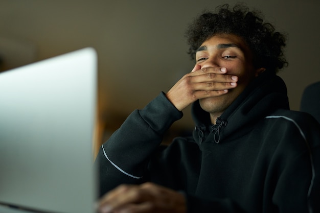 Fatigue somnolent jeune homme tenant la main sur sa bouche tout en bâillant un étudiant étudiant à l'aide